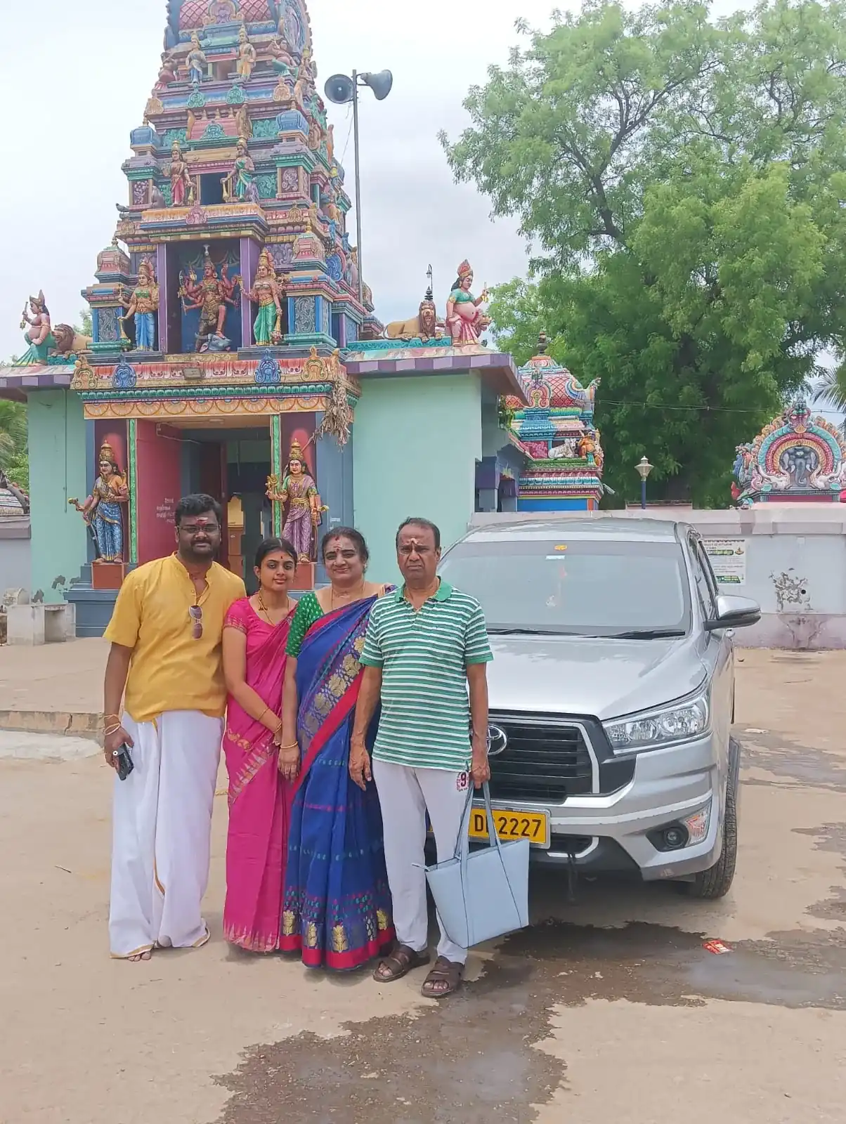 Family standing beside a silver Innova Crysta outside a South Indian temple on a pilgrimage tour